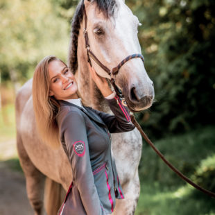 Schöne Frau mit Schimmel Pferd und modernem Turnierjacket in Grau